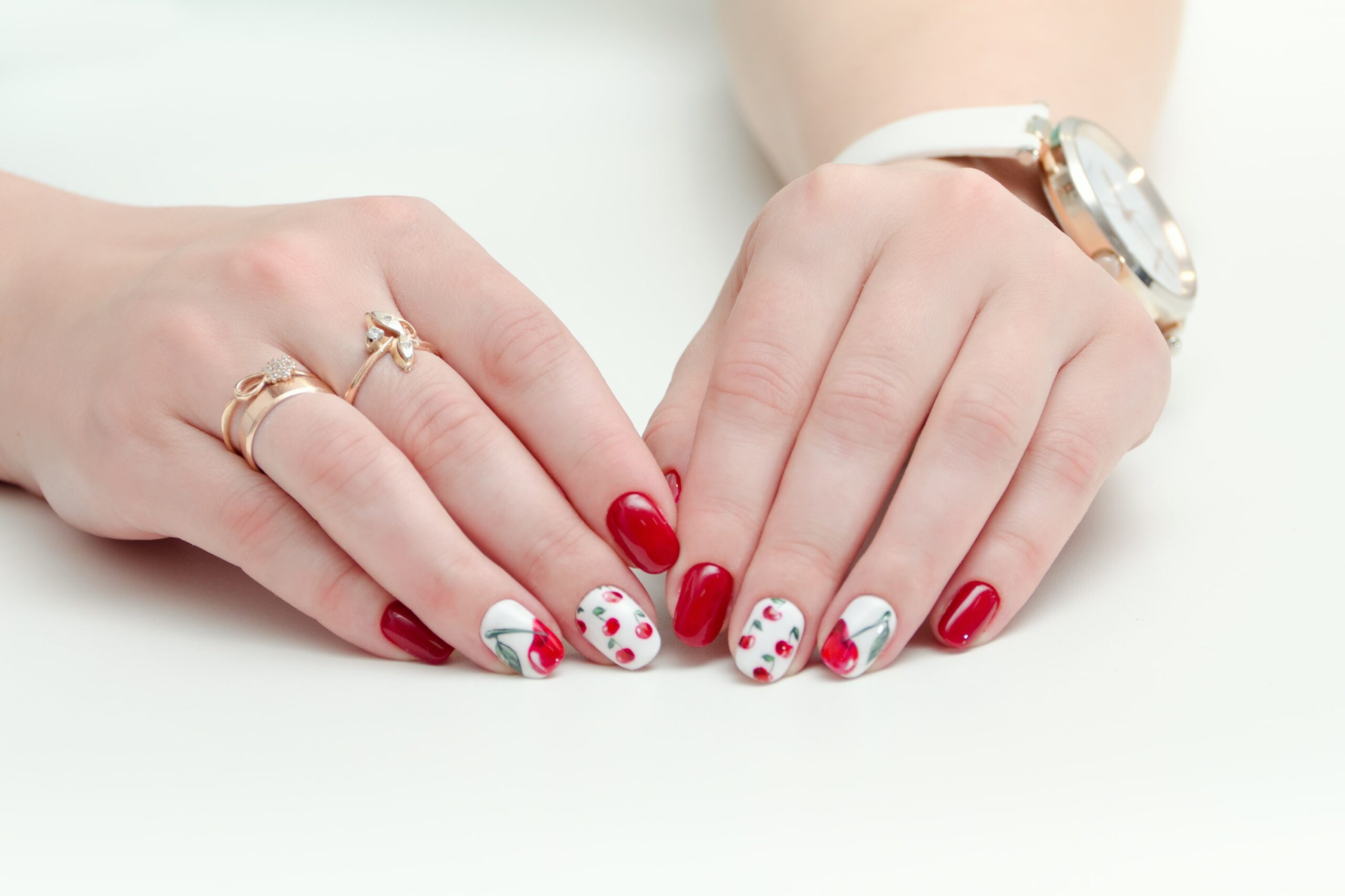female-hands-with-manicure-red-nail-polish-drawing-with-cherries-wrist-watch-white-background-min-scaled.jpg